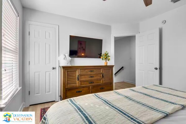 A bedroom with a bed, a dresser, a television, and a door leading to another room.