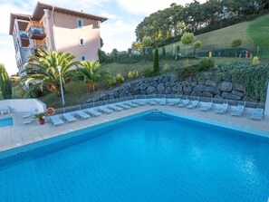 Ein Swimmingpool mit Liegestühlen, einer Steinmauer und einem Gebäude mit Balkonen.