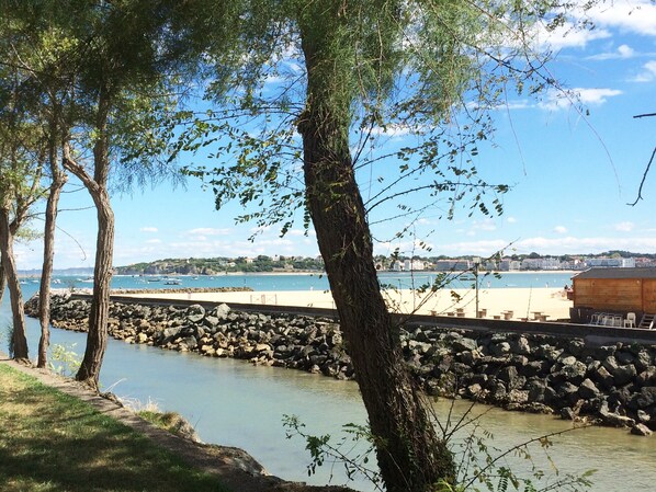 A coastal view with a rocky shoreline, a wooden pier, and a beach area with a wooden structure.