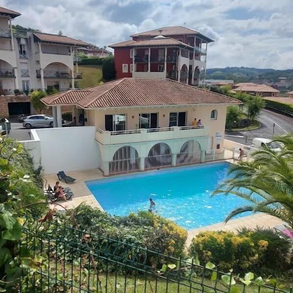 A two-story building with a swimming pool, surrounded by greenery and other residential buildings.