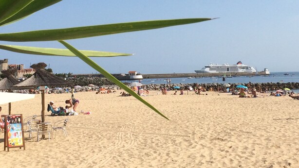 A beach with people, umbrellas, and a cruise ship in the background.