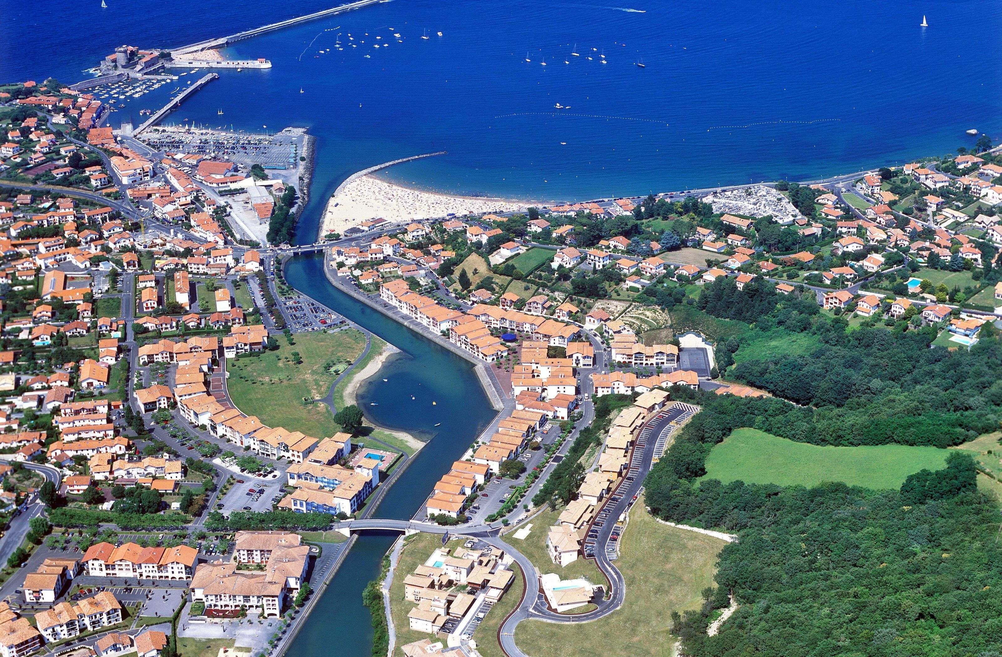 Une vue aérienne d’une ville côtière traversée par une rivière qui se jette dans la mer, les deux étant reliées par un pont.