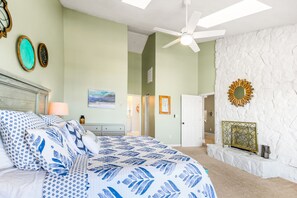 A bedroom with a bed, a ceiling fan, a stone wall, and a door leading to another room. - Beautiful home across from beach with pool, central AC, balcony & washer/dryer (Surfside Beach)