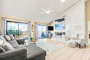 A spacious living room with a grey sectional sofa, a white fireplace, and a stone accent wall. - Beautiful home across from beach with pool, central AC, balcony & washer/dryer (Surfside Beach)