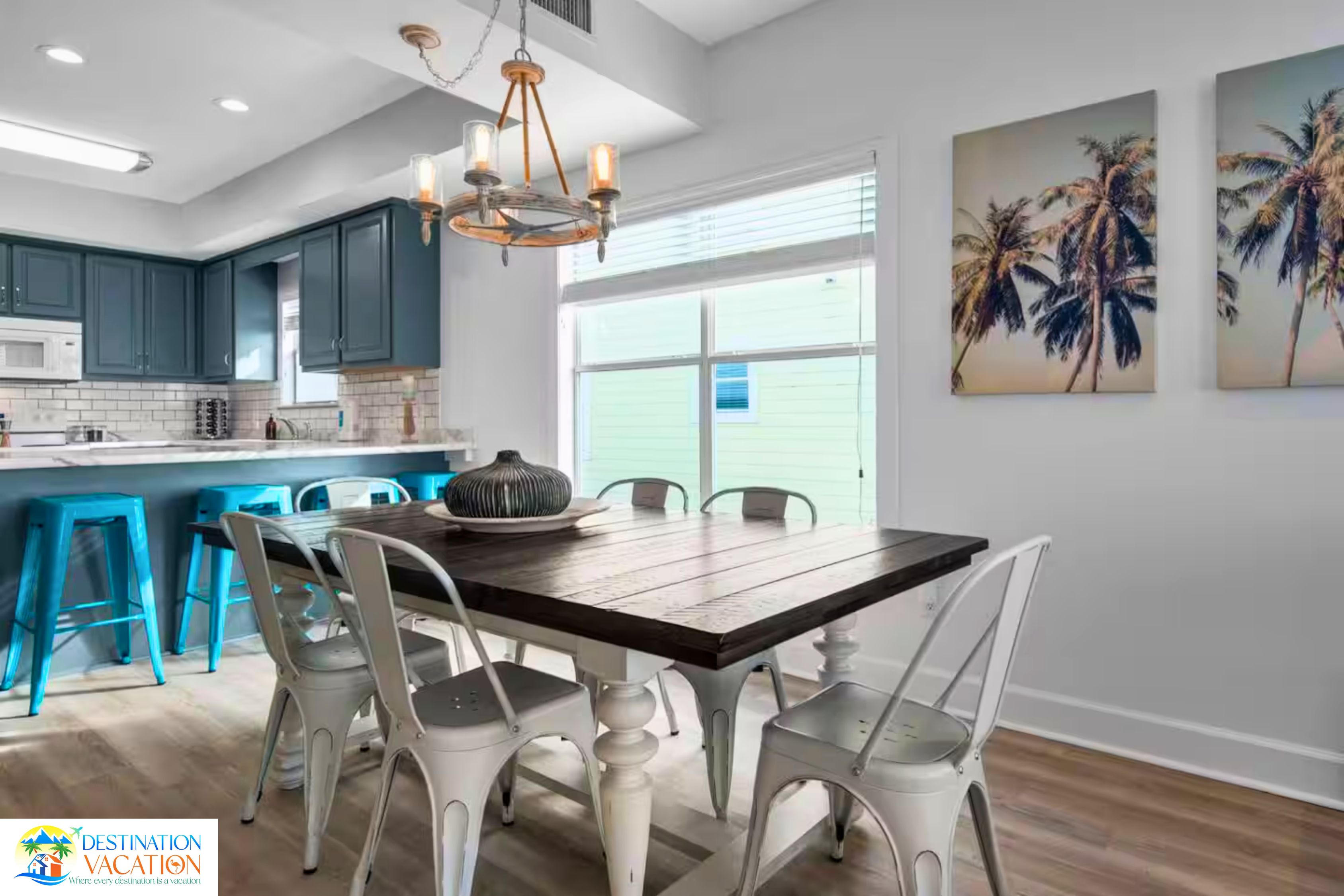 A modern kitchen with teal cabinets, a wooden dining table, and white chairs.