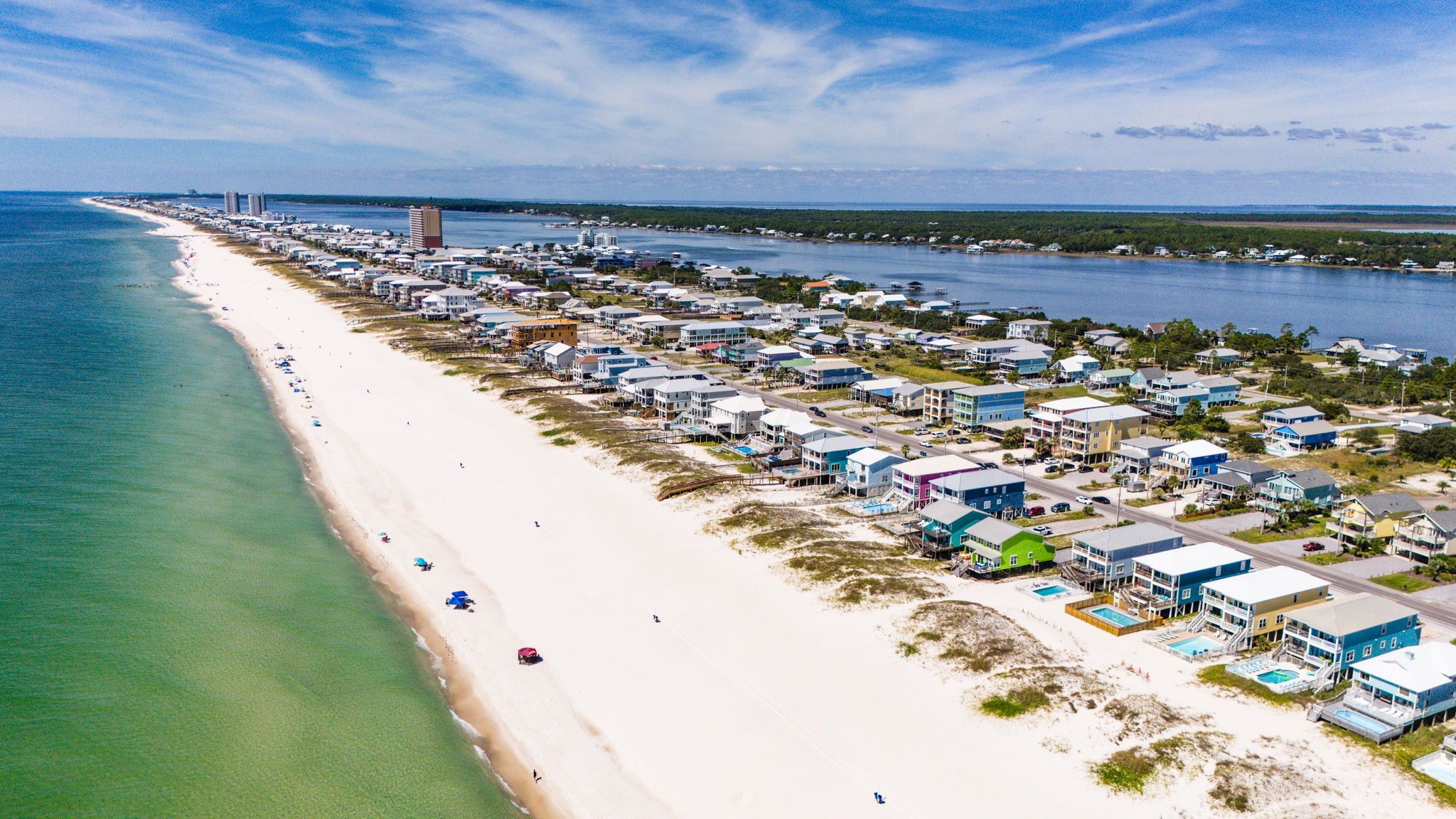 A coastal residential area with beachfront properties, a marina, and a distant bridge.