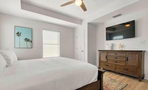 A bedroom with a bed, a dresser, a television, and a ceiling fan. - Gulf Shores Beachfront Gem • 5BR • Pool • Walk to Sand (Gulf Shores)