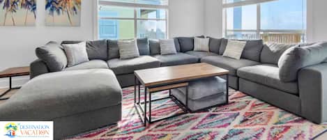 Un salon moderne avec un canapé d’angle, une table basse et un tapis aux couleurs vives.