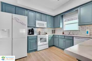 Una cocina moderna con gabinetes azul verdoso, electrodomésticos blancos y piso de madera.