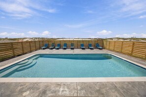 Piscina retangular com cerca de madeira e cadeiras de descanso azuis.