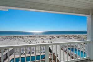 Blick auf den Strand vom Balkon aus, mit Pool und Liegestühlen.