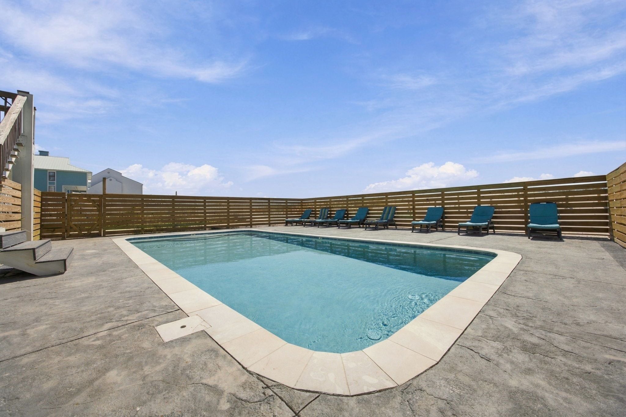 Una piscina rectangular amb vora enrajolada, envoltada per una tanca de fusta i una filera de gandules blaves.