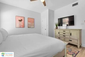 A bedroom with a bed, a dresser, a television, and two wall-mounted pictures.
