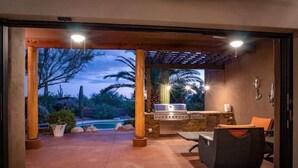 An outdoor patio with a grill, seating, and a view of a pool and trees. - Desert Hideaway+Shuffleboard Court+Golf+Billiards (Scottsdale)