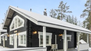 A black wooden cabin with a white porch and a small table. - Rapsakka a by Interhome (Kittilä)