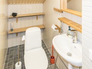 Une petite salle de bain propre, équipée de toilettes, d’un lavabo et de deux étagères.