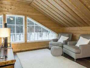 A cozy room with a sloped ceiling, wooden walls, and large windows offering a view of a snowy landscape. - Rapsakka a by Interhome (Kittilä)