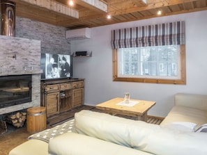A cozy living room with a fireplace, a television, and a window with blinds.