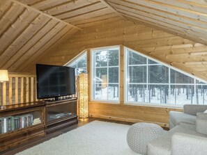 A cozy room with a sloped ceiling, a flat-screen TV, a bookshelf, and a large window with a snowy view. - Rapsakka a by Interhome (Kittilä)