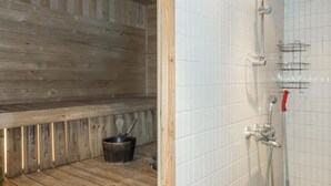 A sauna room with wooden benches, a metal bucket, and a shower area with a hose and a red handle. - Rapsakka a by Interhome (Kittilä)