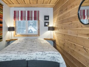 A bedroom with a bed, two bedside lamps, a window with a view, and a mirror on the wall. - Rapsakka a by Interhome (Kittilä)