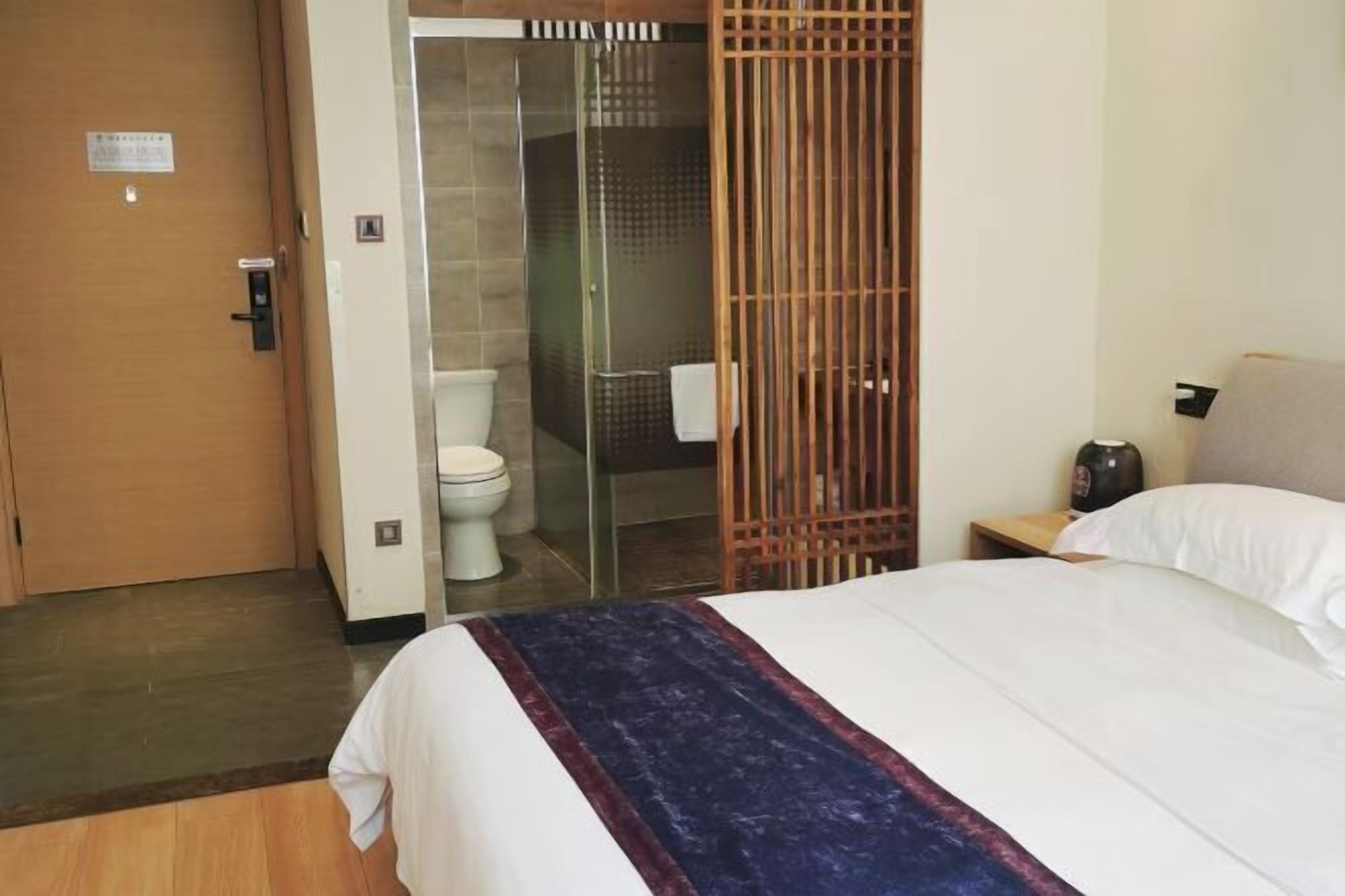 A hotel room with a bed, a wooden door, a toilet, and a shower area.