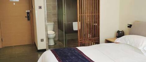 A hotel room with a bed, a wooden door, a toilet, and a shower area.