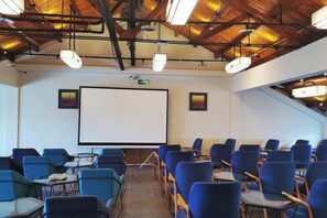 A conference room with a large screen, blue chairs, tables, and a wooden ceiling. - Puchuan Hotel (Tongxiang)