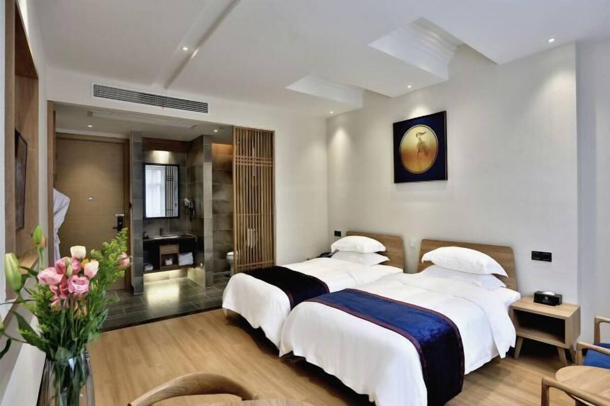 A hotel room with two beds, a bathroom, and a large window.