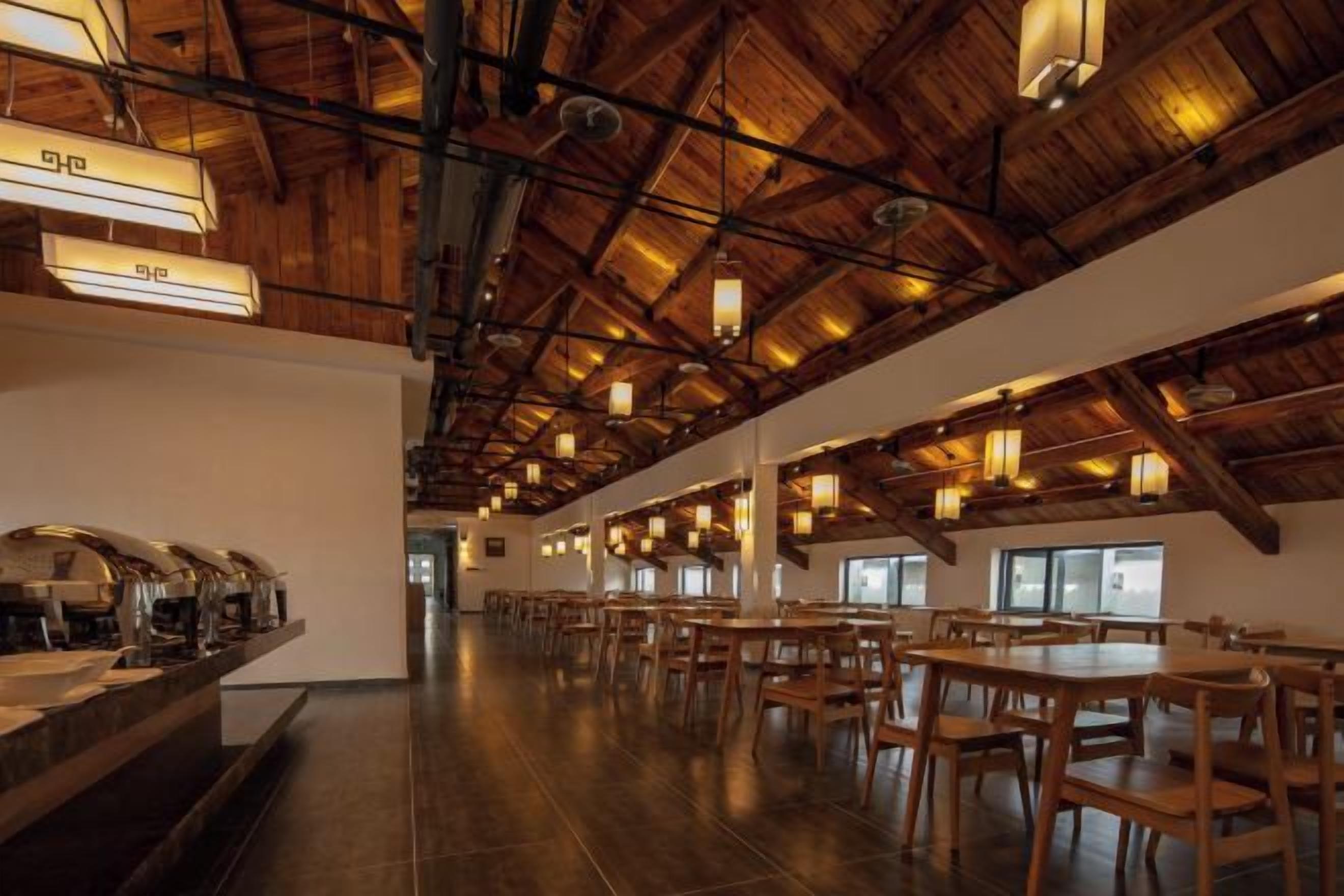A spacious dining area with high ceilings and exposed beams, featuring multiple tables and chairs.
