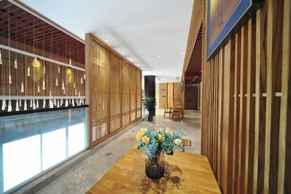 A modern interior with a wooden reception desk, a vase of flowers, and a pool area. - Puchuan Hotel (Tongxiang)