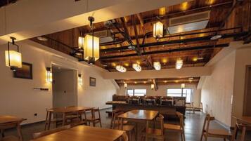 A spacious dining area with high ceilings and exposed beams, featuring multiple tables and chairs.