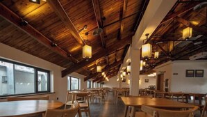 A spacious dining area with wooden tables and chairs, large windows, and exposed wooden beams on the ceiling. - Puchuan Hotel (Tongxiang)