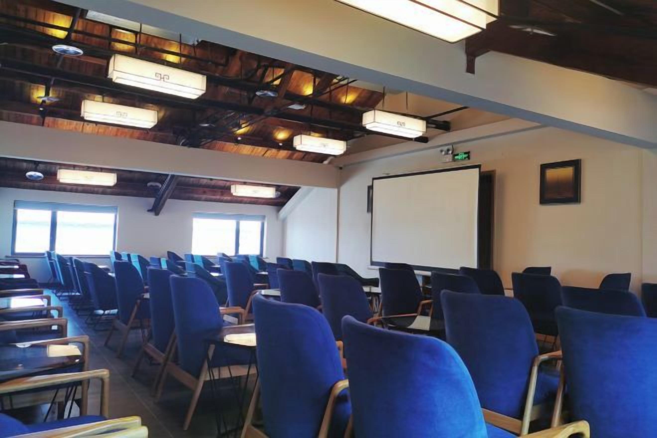 Une salle de conférence avec des rangées de chaises, un écran de projection et un tableau blanc.
