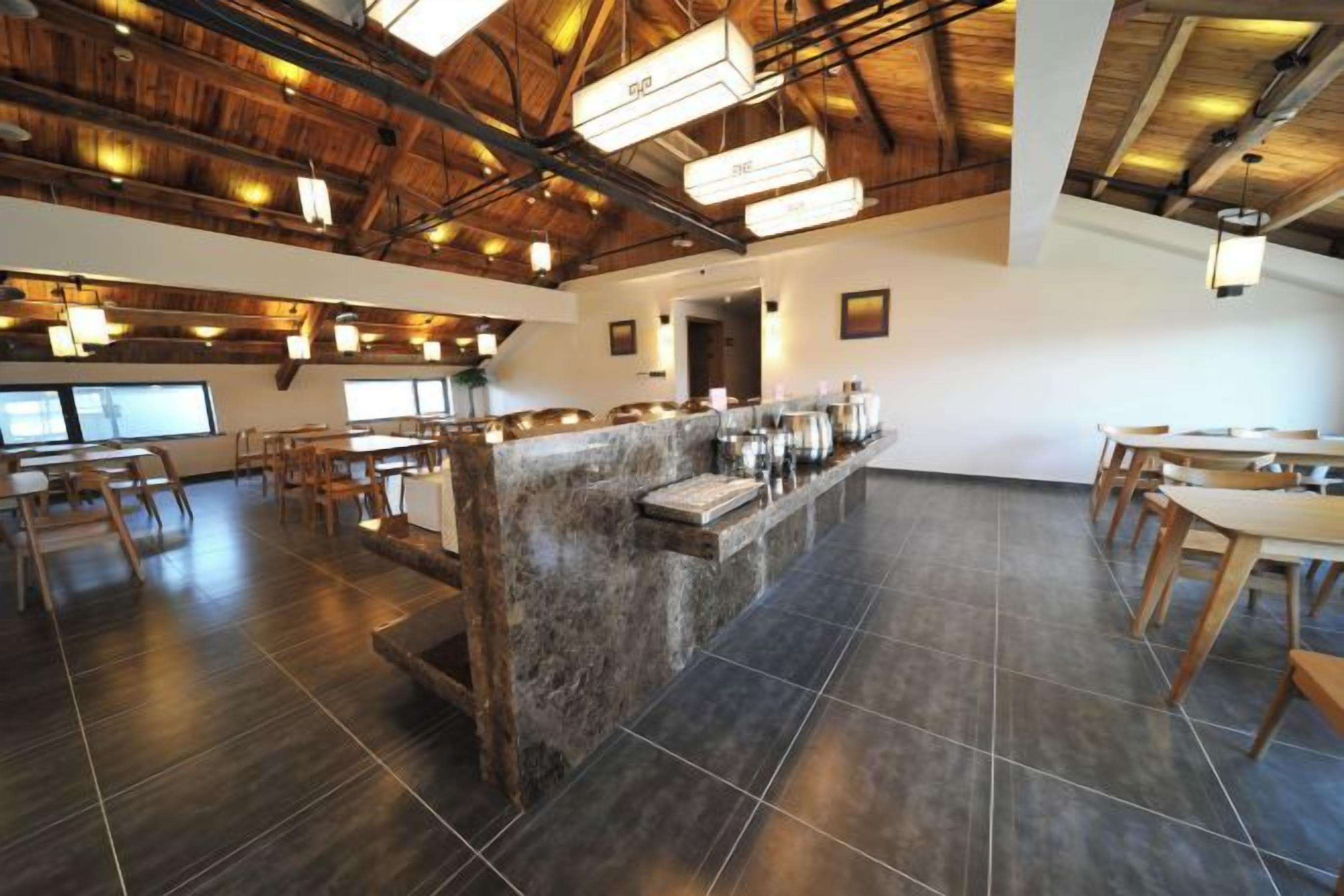 Ein geräumiges Restaurant mit hoher Decke, Holzbalken und einer zentralen Bar.