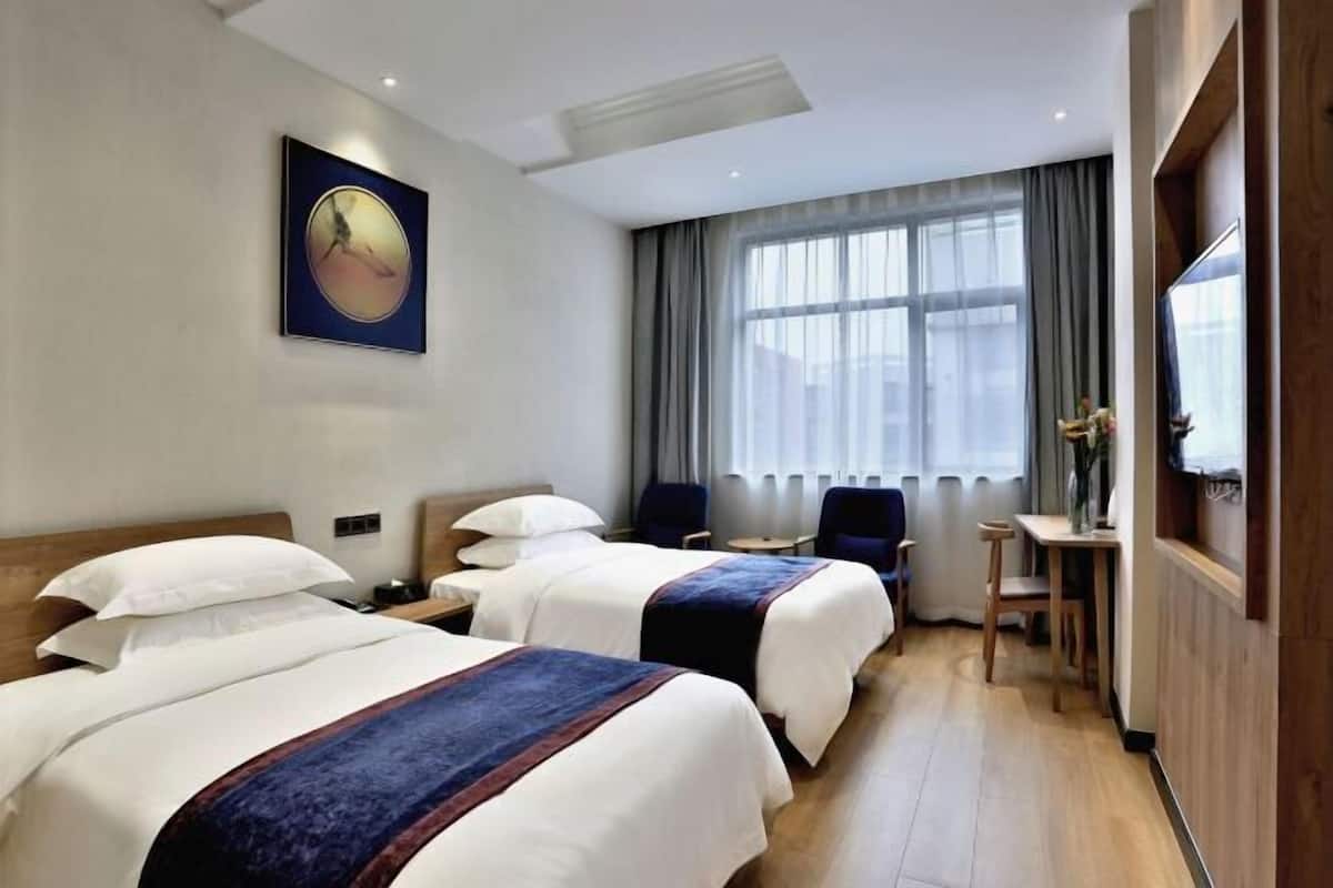 A hotel room with two beds, a desk, a chair, a TV, and a large window with curtains.