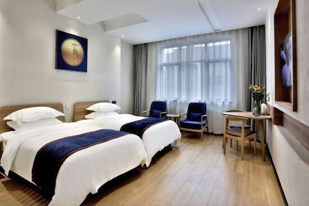 A hotel room with two beds, a desk, chairs, and a large window with curtains.