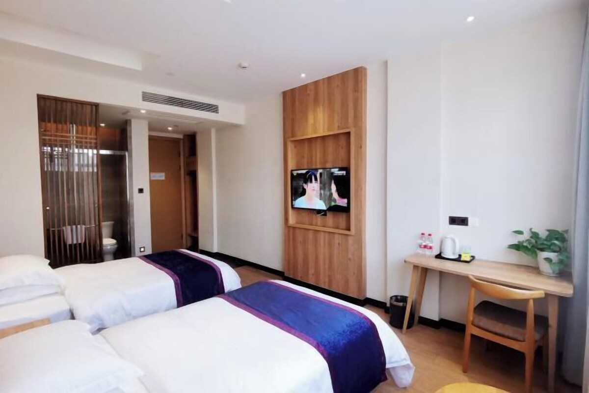 A hotel room with two beds, a TV, a desk with a chair, and a small table with a plant.