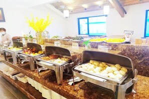 A buffet setup with various food items and a person in the background. - Puchuan Hotel (Tongxiang)