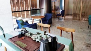 A modern lounge area with a table set for tea service, featuring a teapot, cups, and a tray. There are chairs and a sofa in the background. - Puchuan Hotel (Tongxiang)