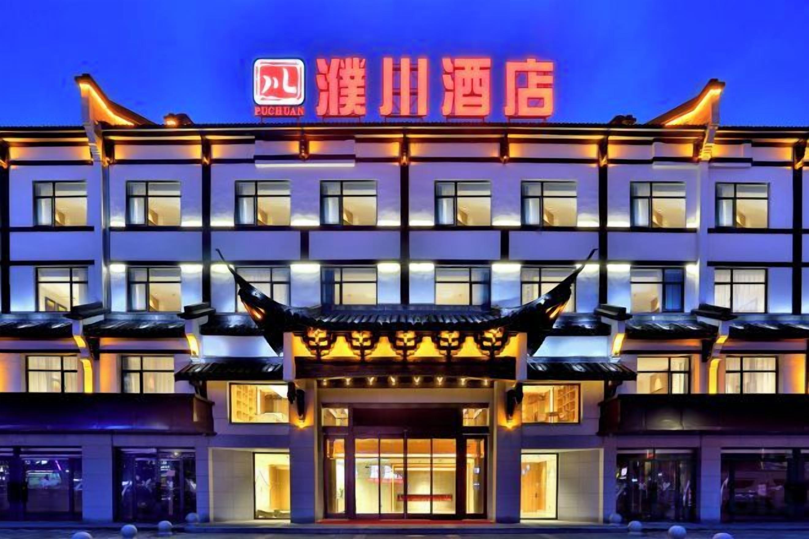 A hotel with a traditional architectural style, featuring a prominent entrance with a decorative roof and illuminated signage.