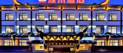 Un hotel de estilo arquitectónico tradicional, con una entrada destacada, techo decorativo y señalización iluminada.