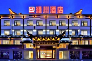 A hotel with a traditional architectural style, featuring a prominent entrance with a decorative roof and illuminated signage. - Puchuan Hotel (Tongxiang)