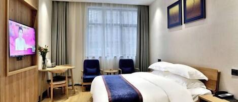 A hotel room with a bed, a TV, a desk, two chairs, and a window with curtains.