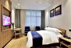 A hotel room with a bed, a TV, a desk, two chairs, and a window with curtains. - Puchuan Hotel (Tongxiang)
