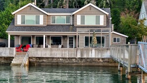 A two-story house with a balcony, a dock extending into a body of water, and a small deck area.