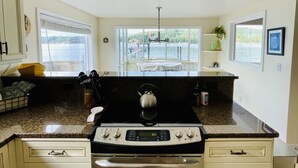 A kitchen with a stove, oven, and granite countertops. There are windows with a view of a lake and a balcony with a table and chairs.