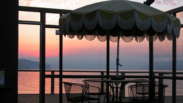 A deck with a table and chairs, an umbrella, and a view of the water at sunset.