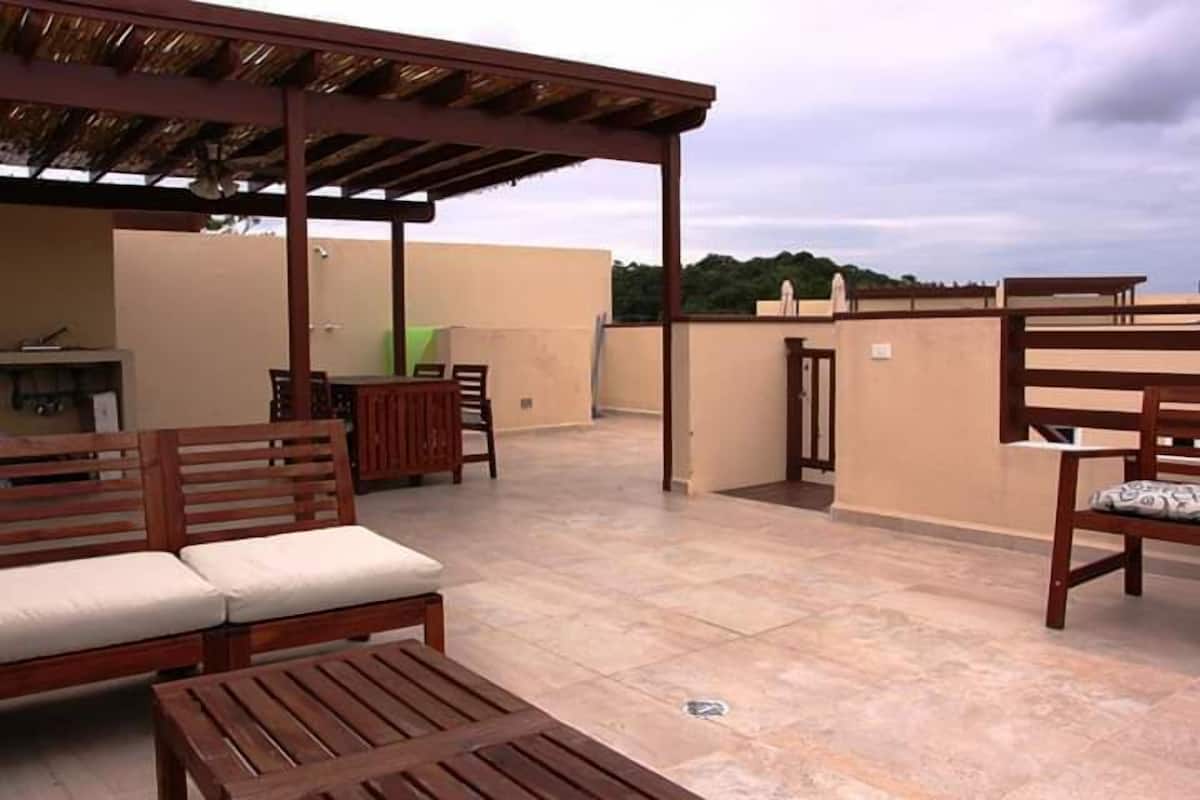 An outdoor patio area with wooden furniture, including a sofa and a table, under a pergola.