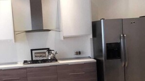 A modern kitchen with a stainless steel refrigerator, dark wooden cabinets, and a white countertop. - Estudio in Las Palmas (Roatan)